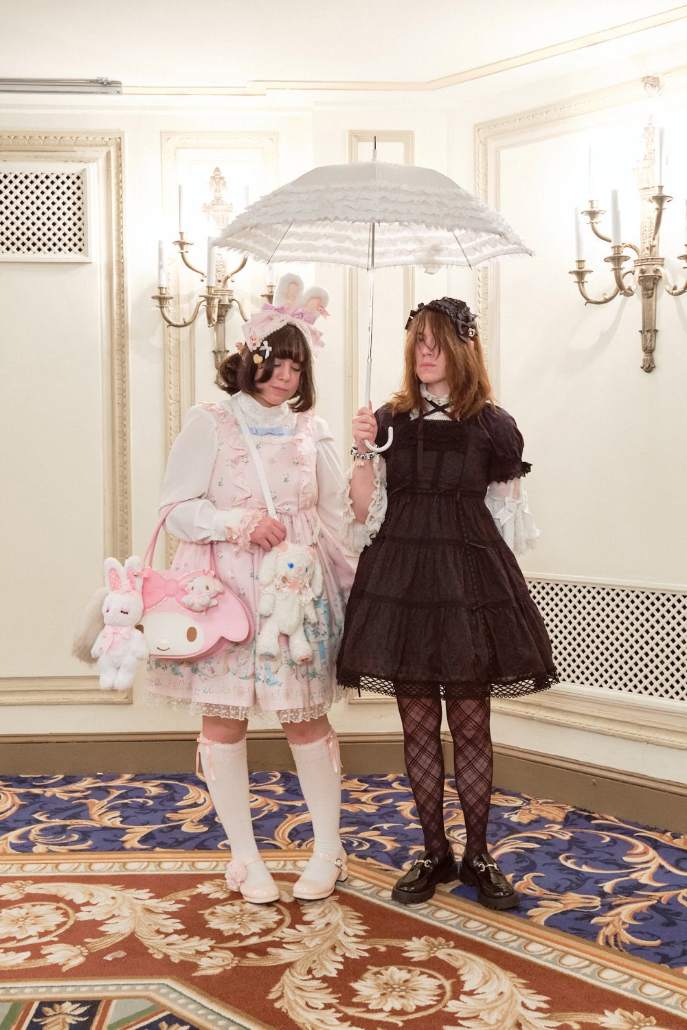 Two sweet lolitas standing together. Left one wore a bunny themed pink outfit. Black one wore a simple black dress with white blouse.