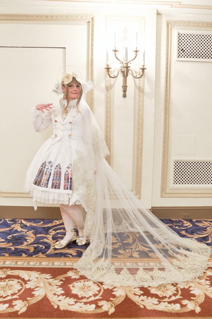 White wearing lolita wearing angelic themed outfit with stain glass dress, halo, and long lace train.