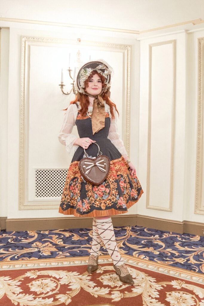 Classic lolita wearing navy and red floral print dress, ornate bonnet and brown heart bag,