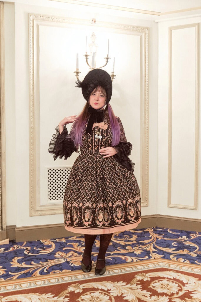 Classic lolita wearing ornate princess themed dress with large black bonnet.