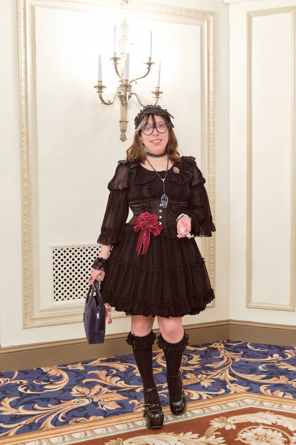 Gothic lolita wearing all black with a pop of color from a single red rose brooch.