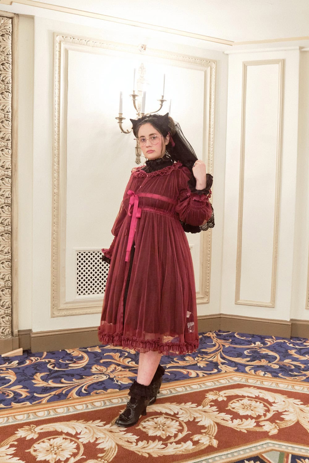 Gothic lolita wearing bat headdress, black blouse, and red tulle peignoir.