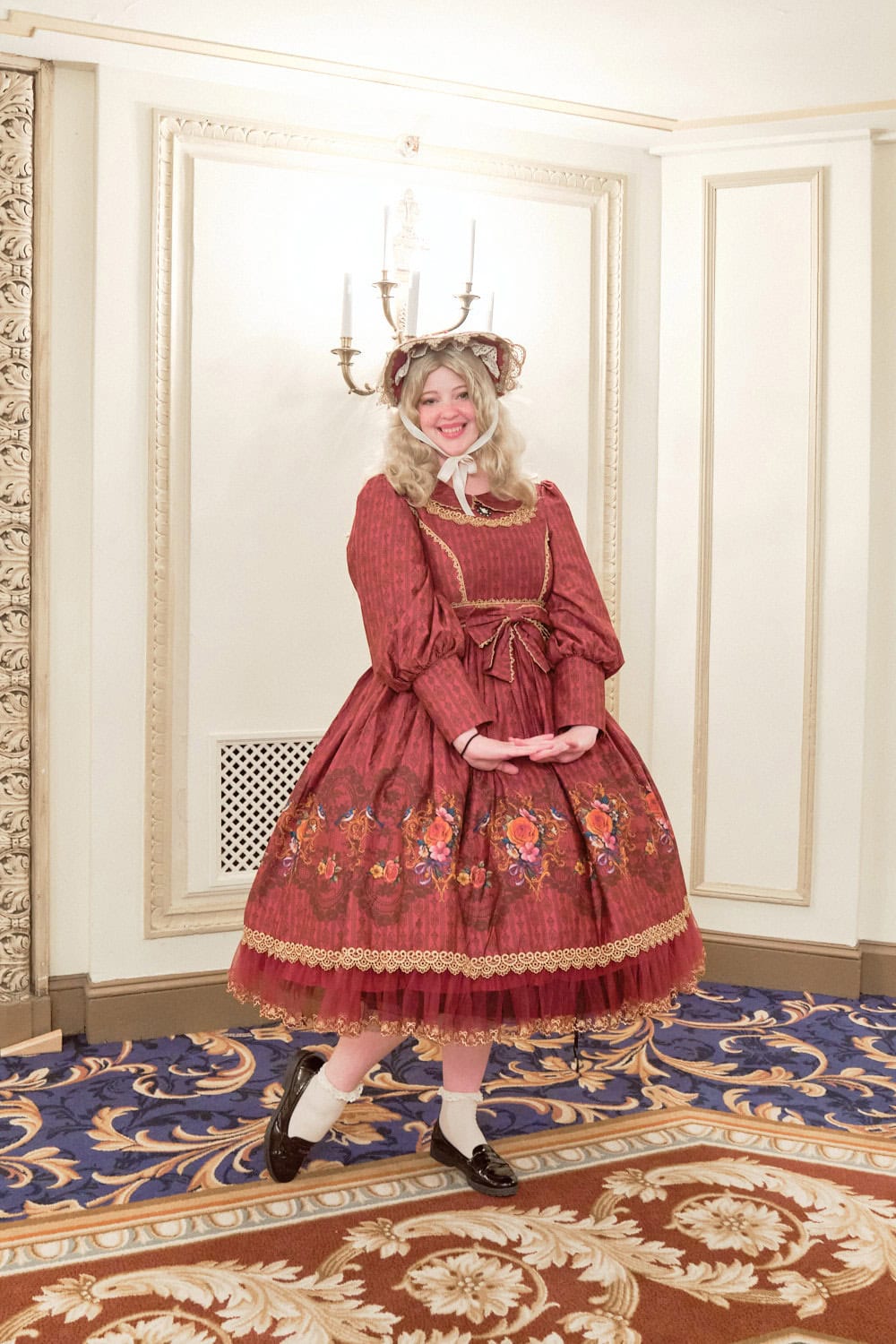 Classic lolita wearing red and gold colored bonnet and dress. The dress has a floral border print.