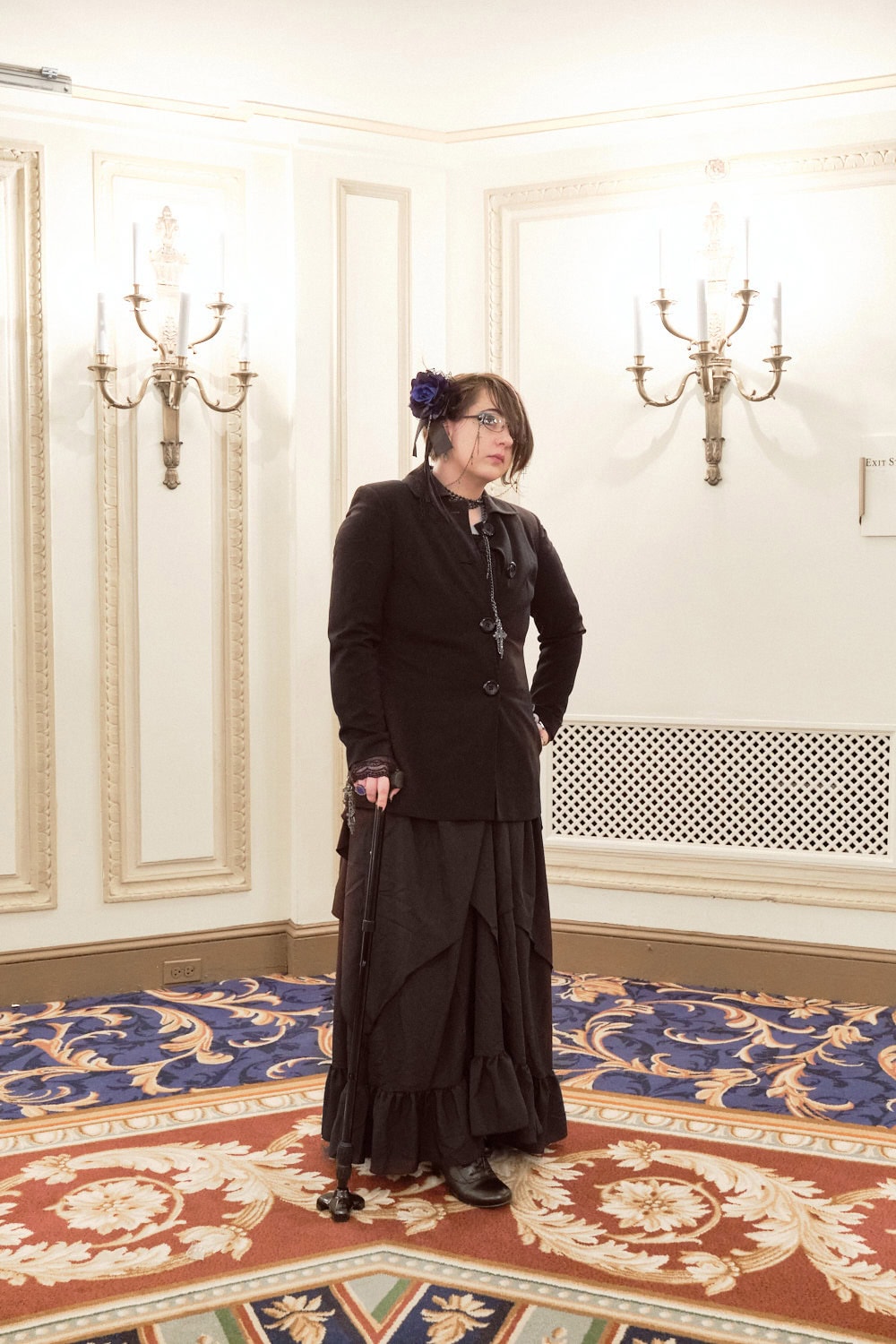 Gothic aristocrat wearing black blazer with wide long pants and holding cane.
