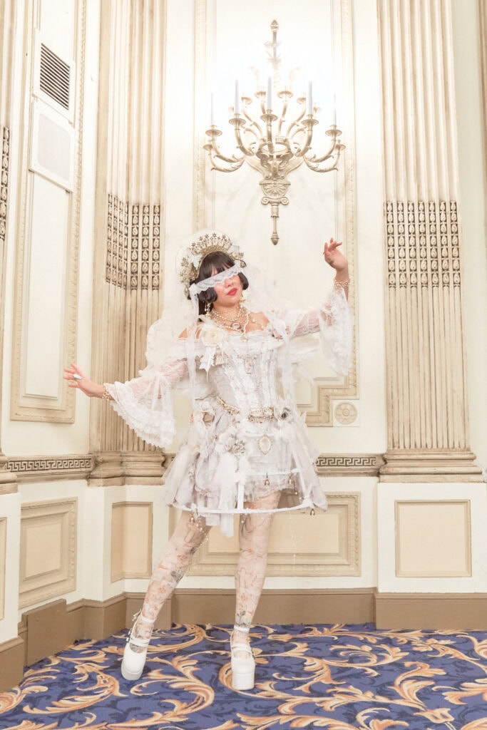 Lolita wearing angel themed white outfit featuring multiple intricate gold accessories.