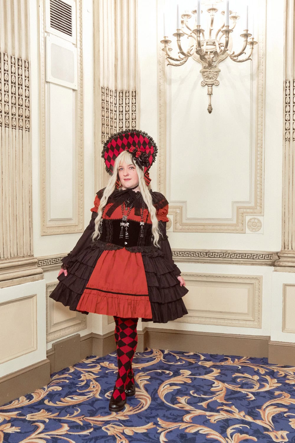 Gothic lolita wearing black and red themed outfit with diamond pattern bonnet and socks.