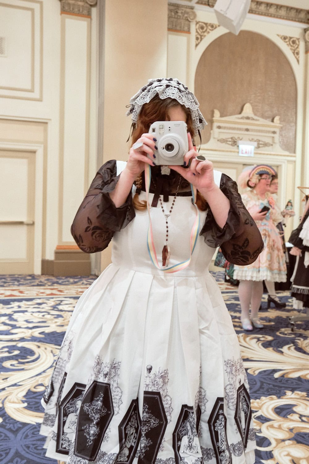 Gothic lolita holding Instax camera up to face.