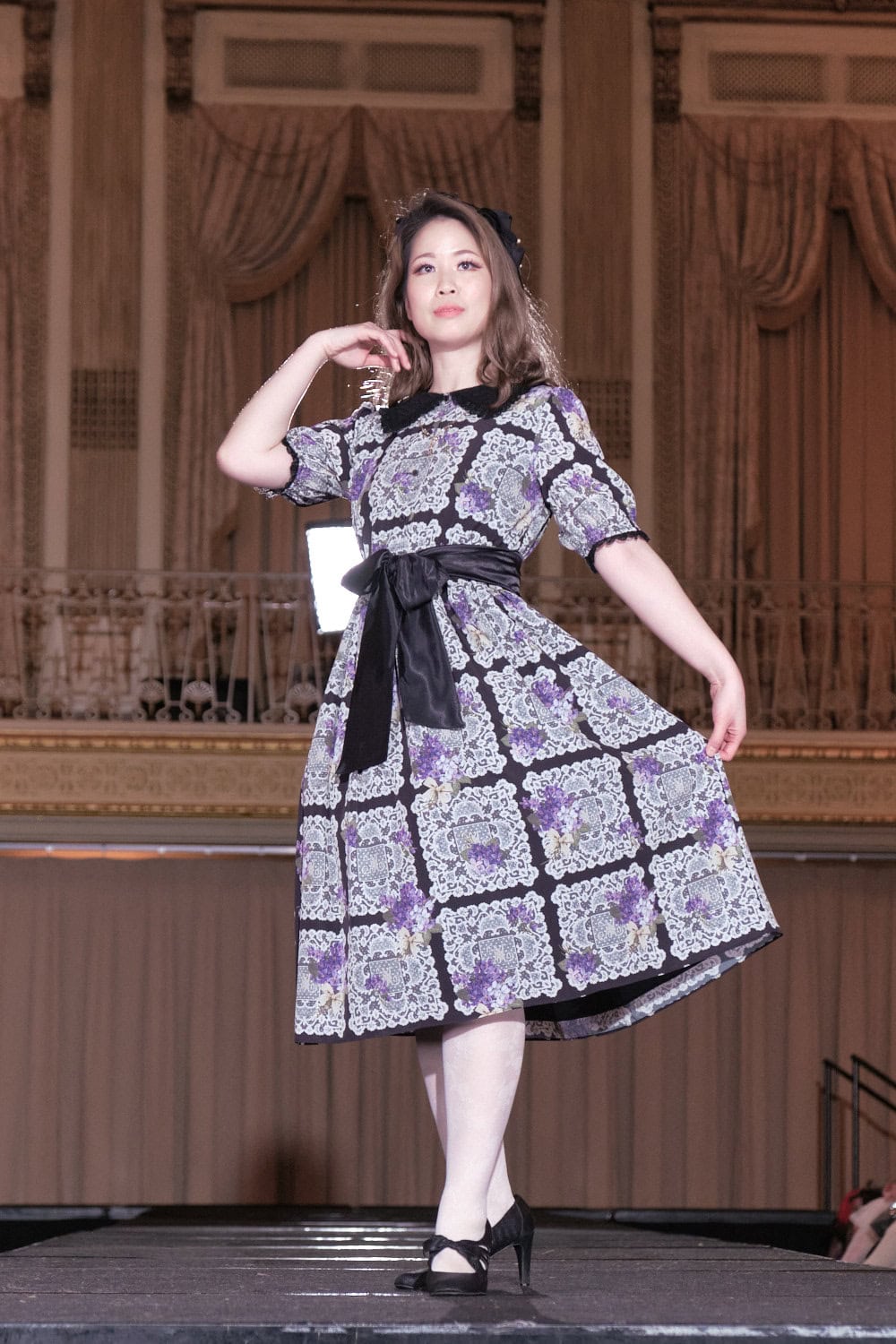 Model 7 wearing black, purple, and white classic lolita dress by Melody Basket. The dress features a lace and violet flower print. The collar and waist ribbon are solid black.