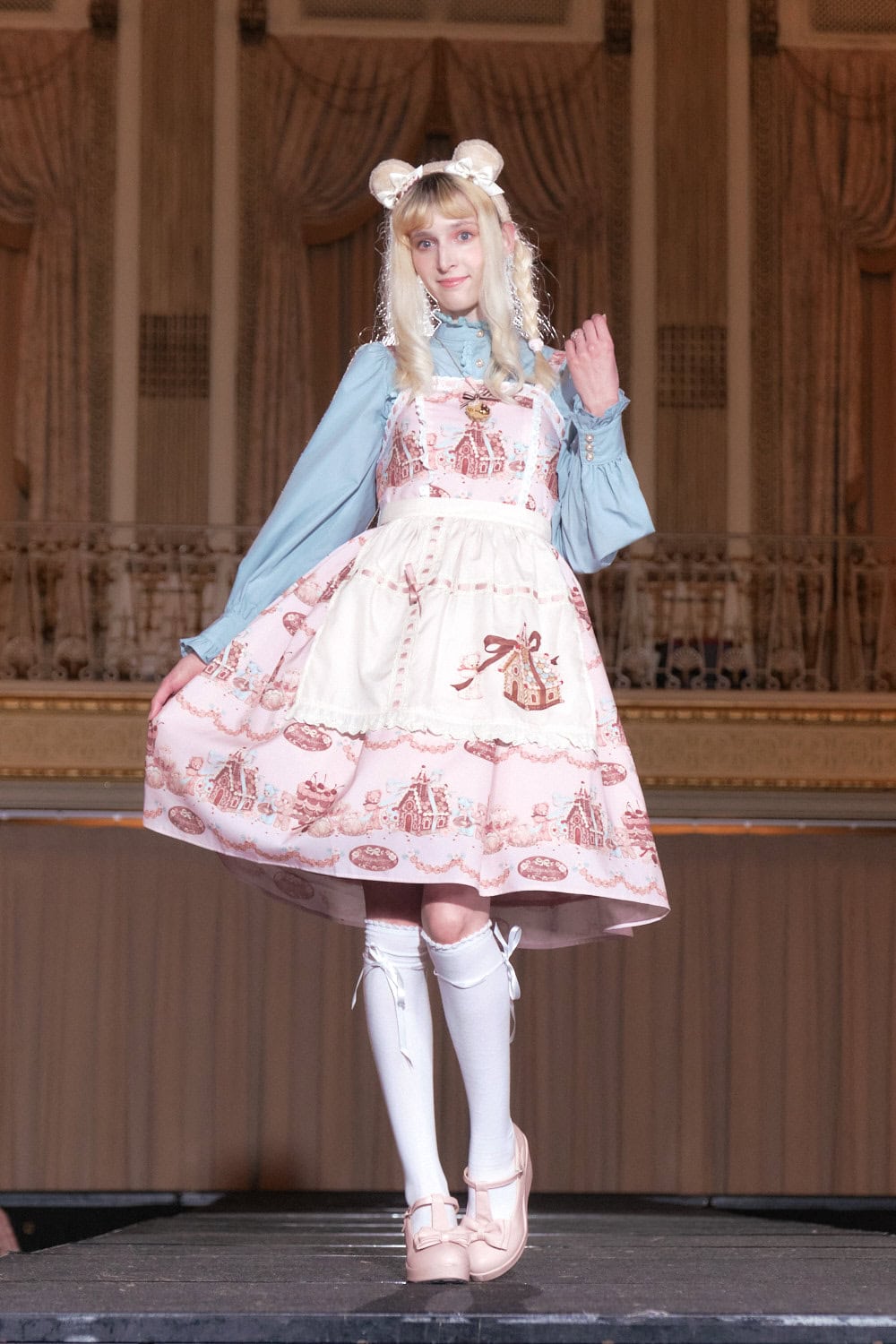 Model 11 wearing pink gingerbread themed sweet lolita dress with white apron by Axes Femme Kawaii.