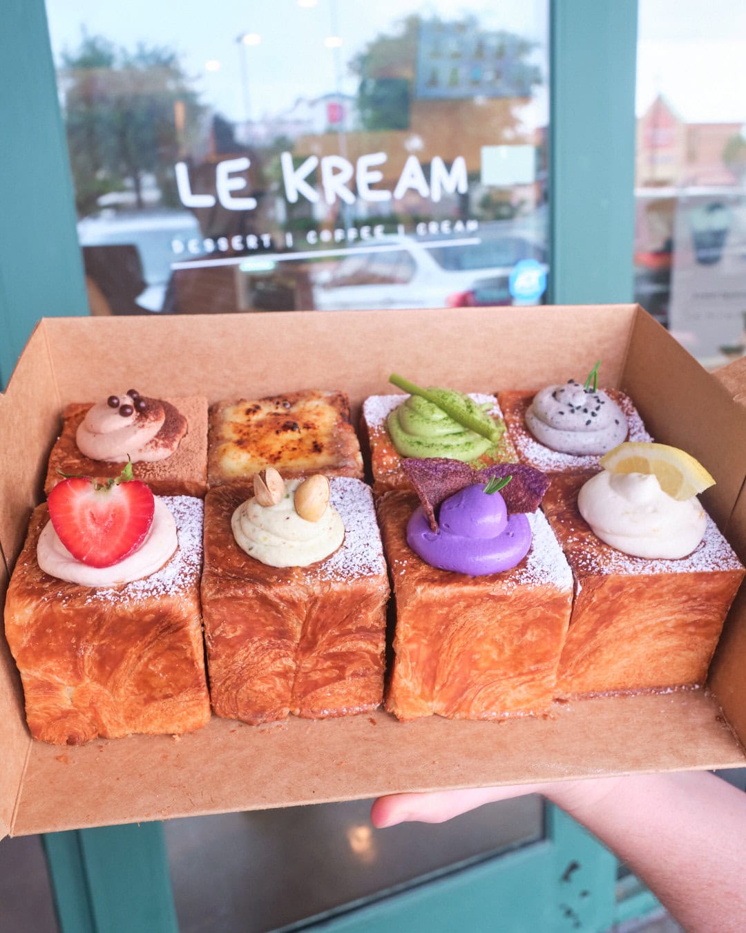Box of 8 cube croissants in front of "Le Kream" storefront door.