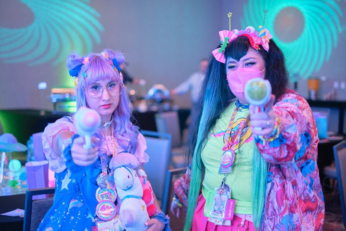 Two friends wearing space themed outfits standing next to each other pointing toy water guns at camera - portrait.