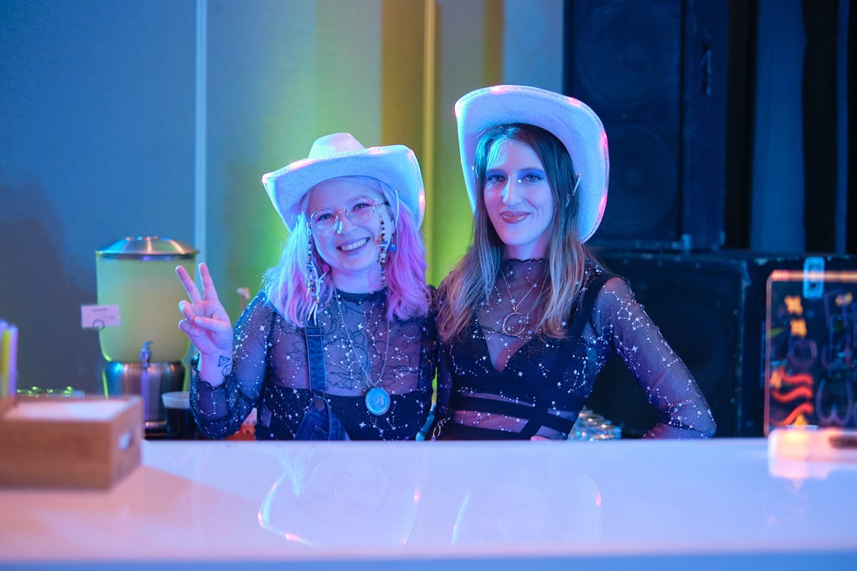 Two bartenders wearing cowboy hats smiling behind counter.