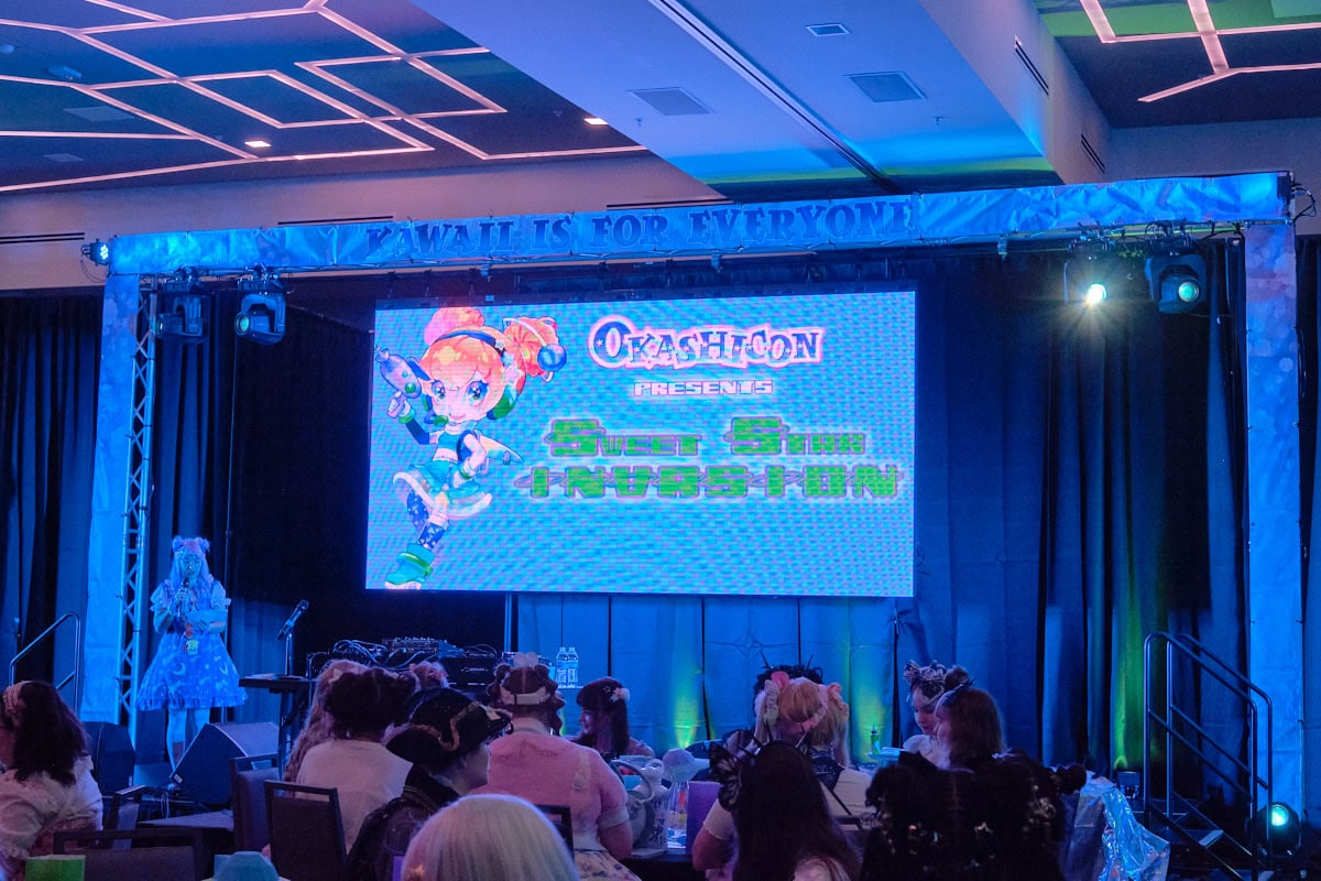 Screen showing anime mascot with text "Okashicon presents Sweet Star Invasion"