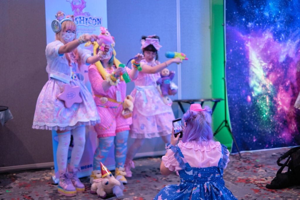 Trio of pastel wearing people posing for photo while a fourth person holds phone to take the photo.