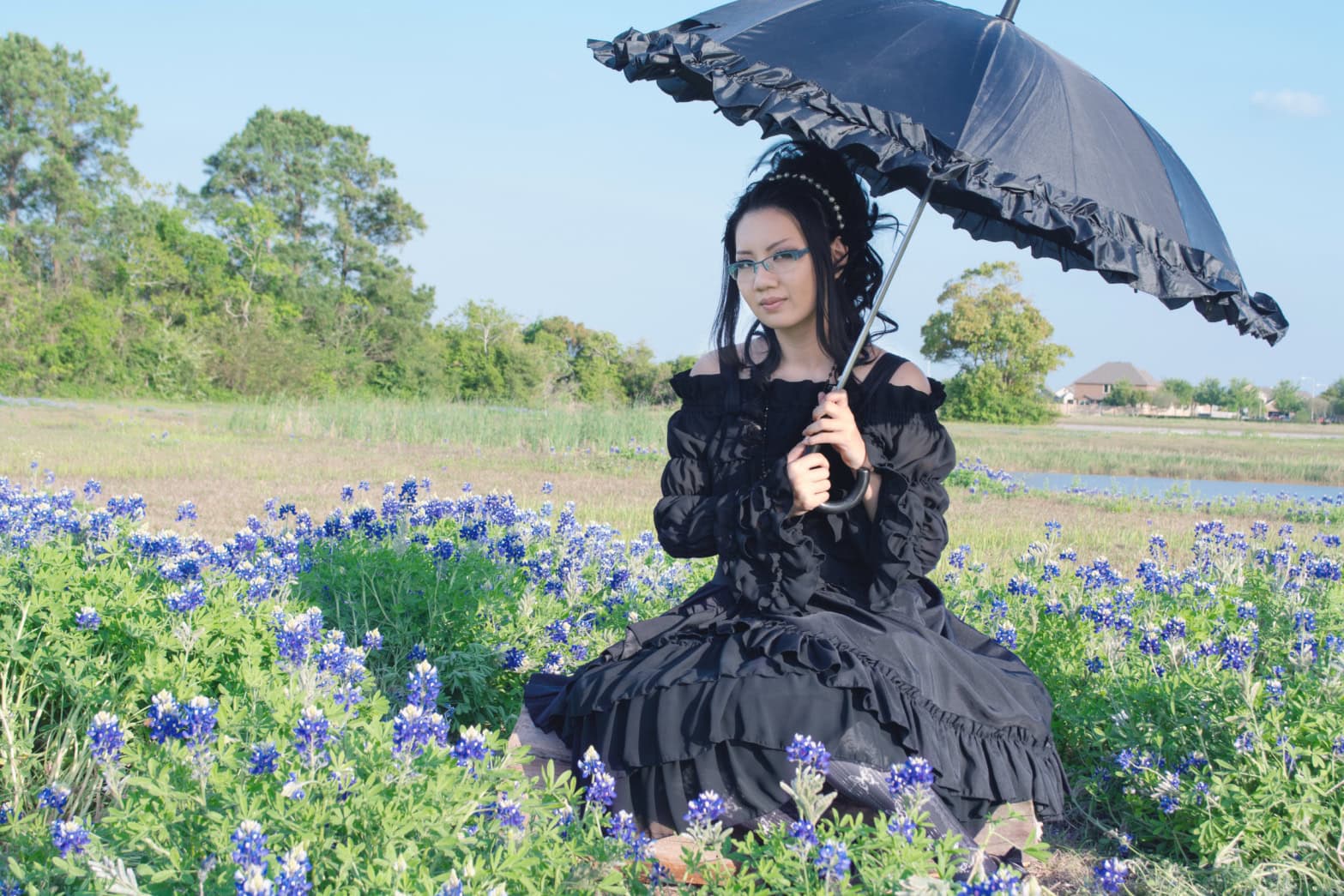 Stephano sitting in a sunny field of bluebonnets. She uses a parasol to shield from the sun.