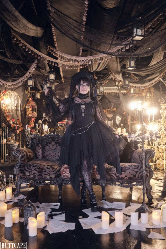 Full body photo of gothic lolita Stephano standing in a gothic themed photo studio.