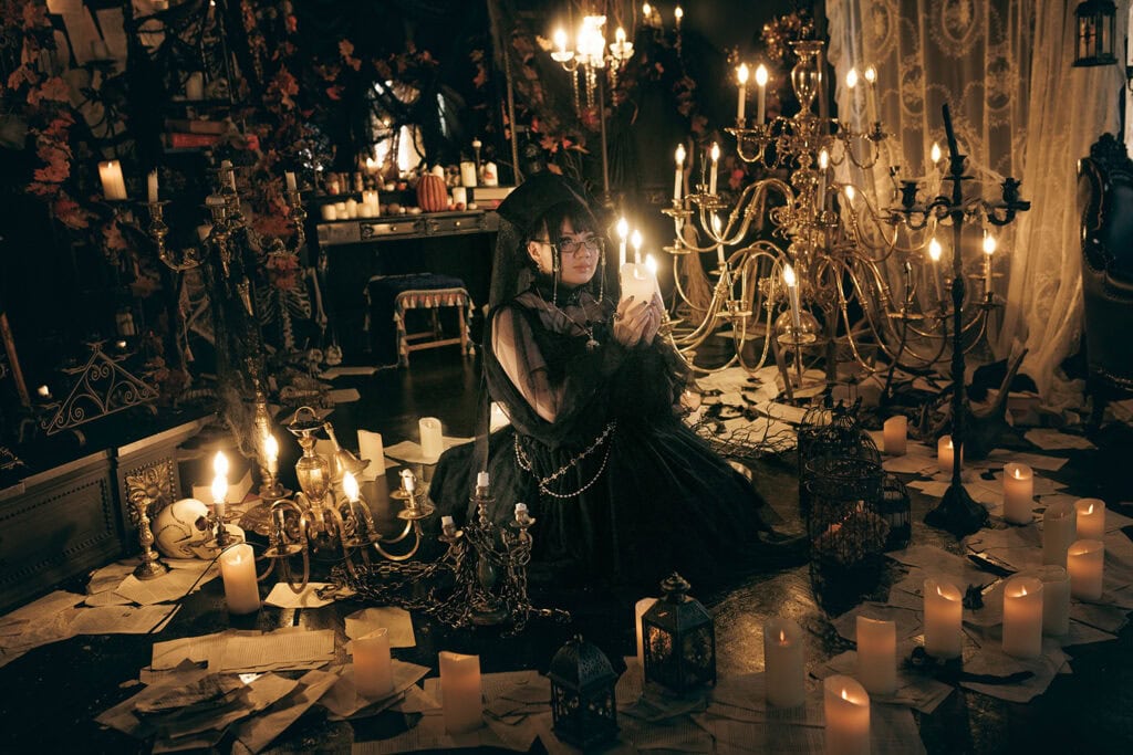 Stephano holding candle in hand. She sits in the middle of a circle of candles, lights, and antiques.