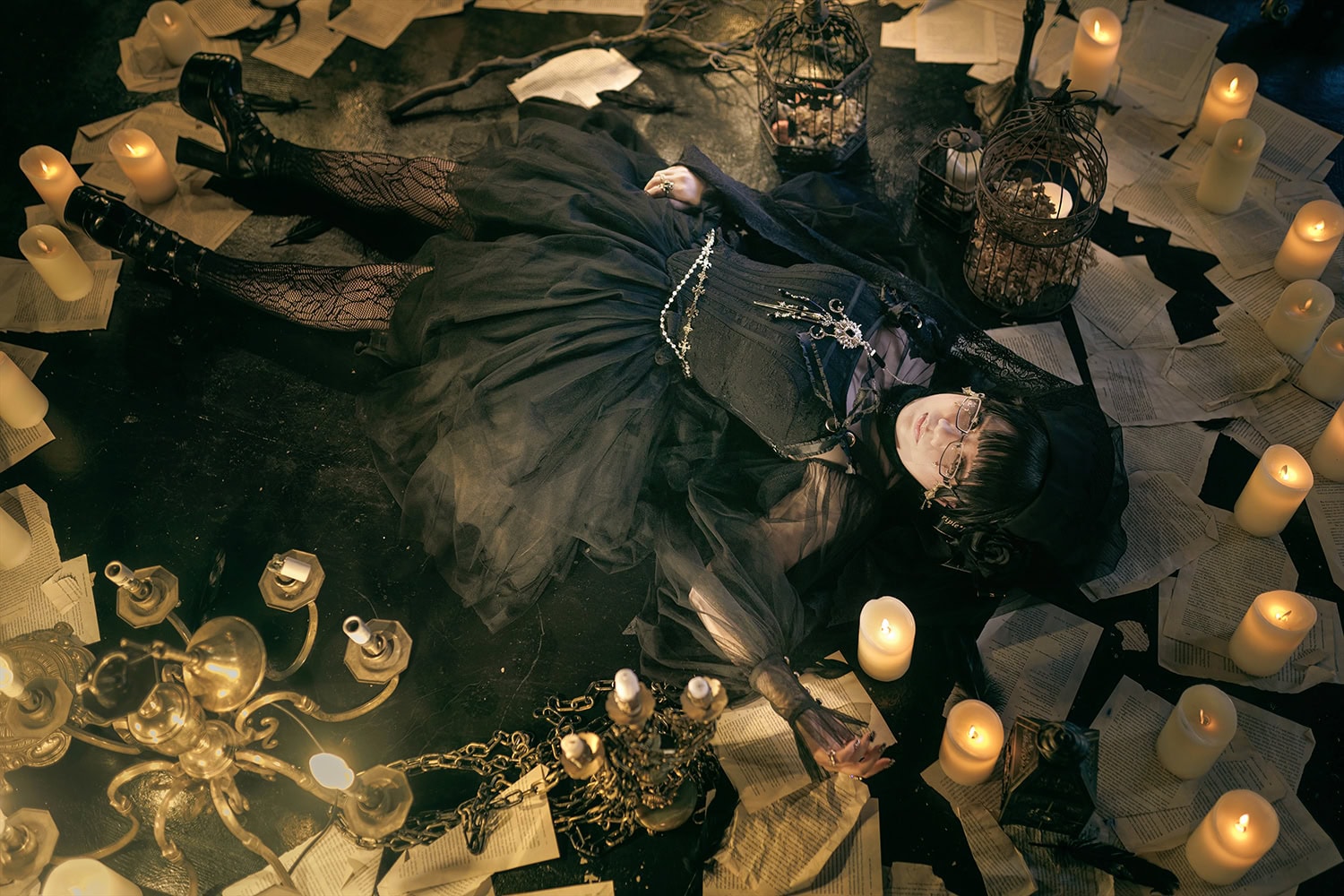 Stephano laying in a pile of book pages, bird cages, and candles.