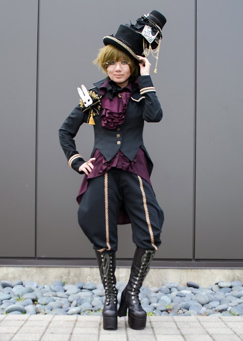Stephano wearing a black, wine, and gold ouji outfit inspired by Alice in Wonderland and the Mad Hatter.