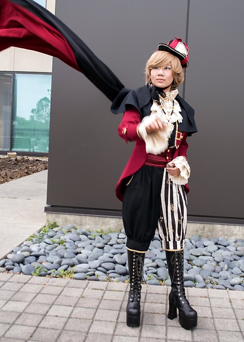 Stephano wearing a black, red, and white outfit inspired by the Mad Hatter. The outfit features a long cape.