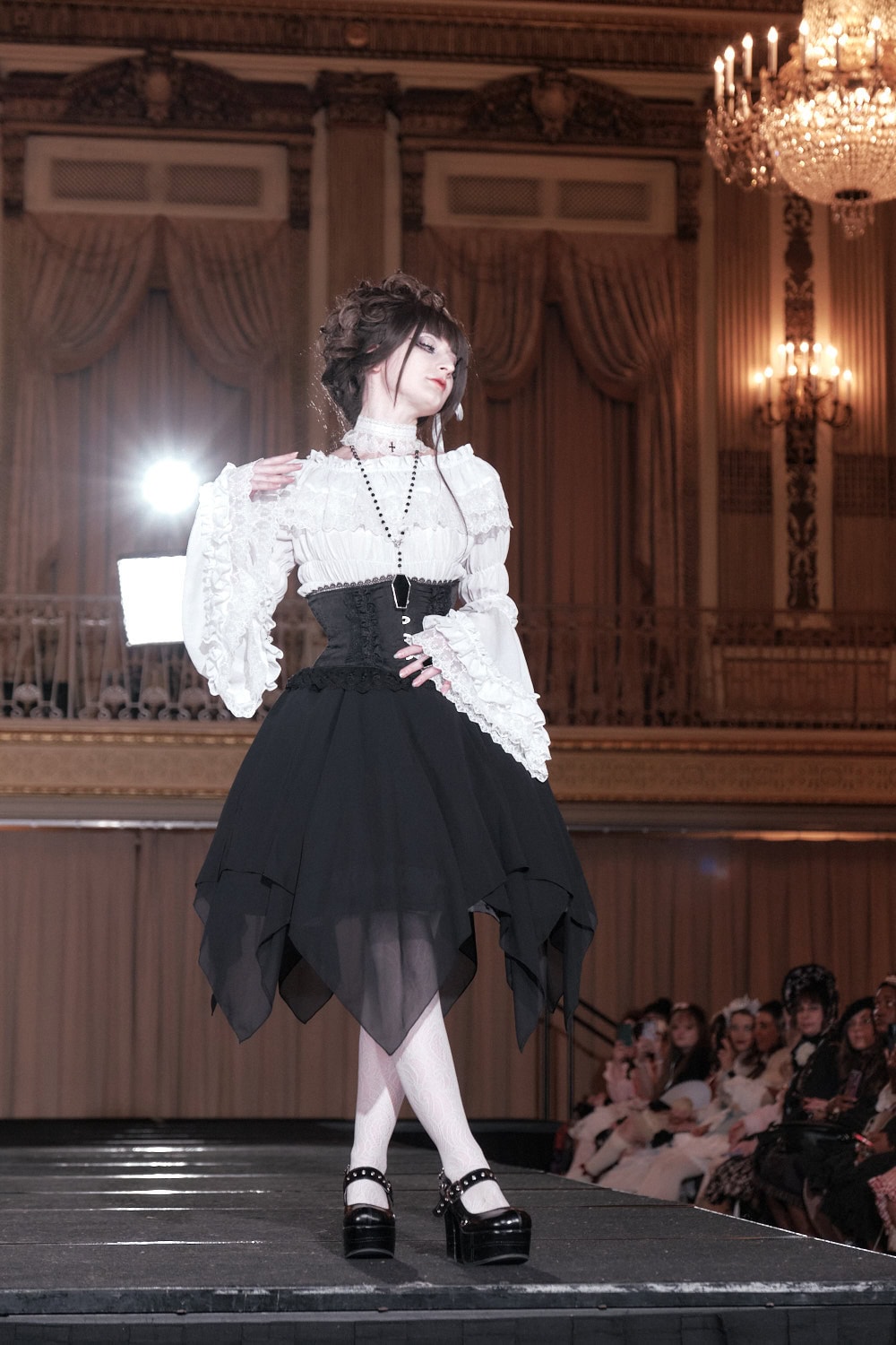 Model 3 wearing a black and white gothic lolita outfit consisting of white choker, white princess sleeve blouse, and white stockings. The outfit is paired with black waist corset, black handkerchief hem skirt, black rosary necklace, and black platform shoes.
