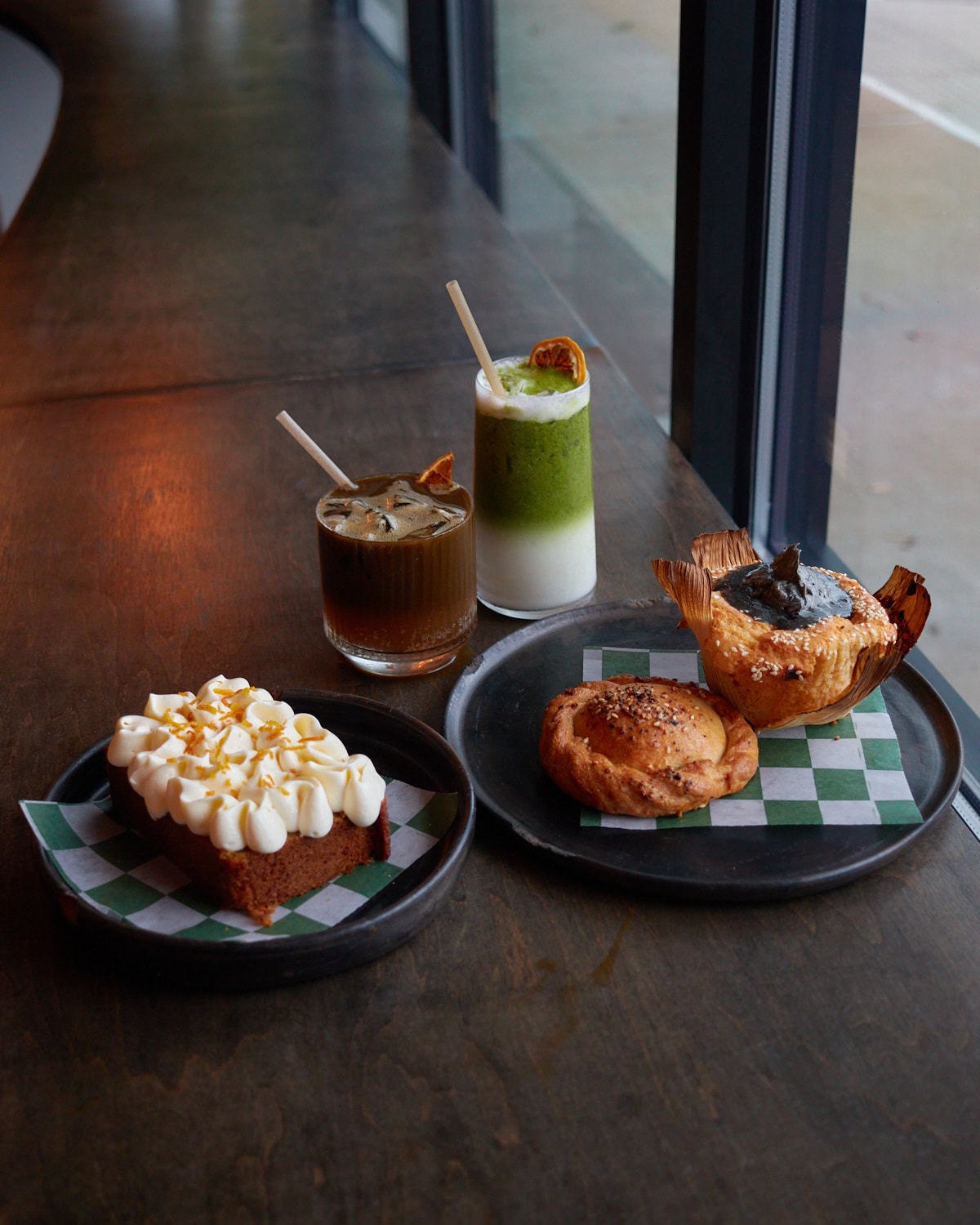 third place matcha latte and houjicha cowboy drink next to a carrot cake slice, black sesame bread, and filled bread