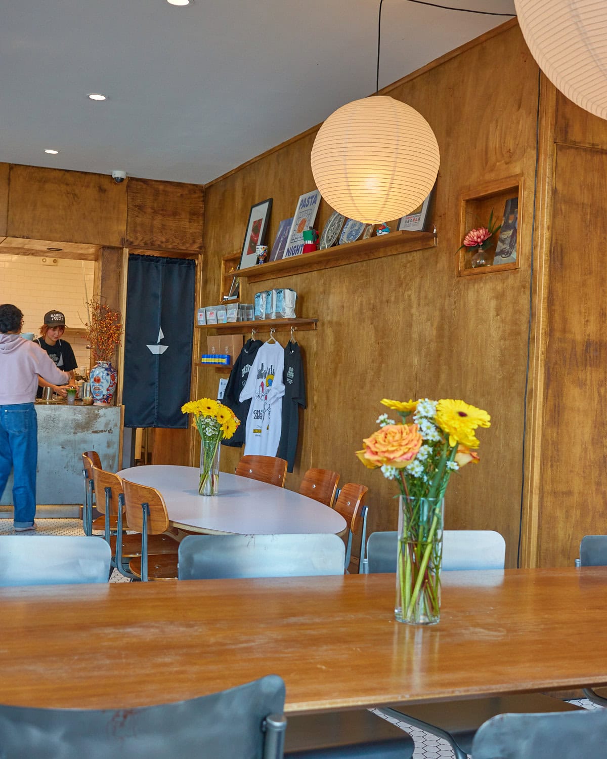 wood clad walls in a coffee shop with orange and yellow flowers on a large wooden communal table