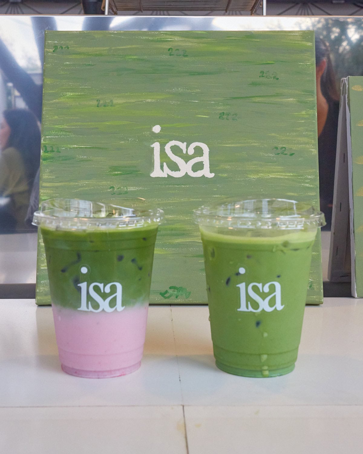 isa matcha latte and strawberry matcha latte in front of isa sign