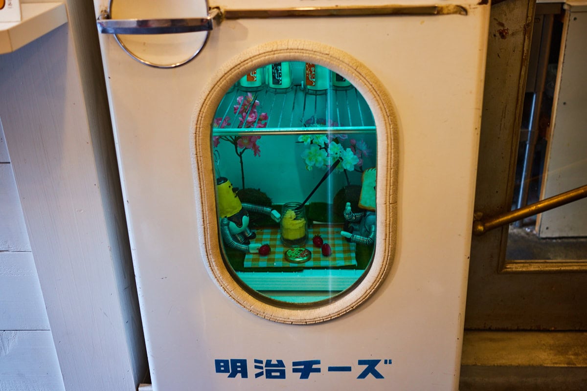 Retro Meiji Cheese refrigerator that has been transformed into an art piece featuring pudding and pudding toast characters having a picnic and sharing a pudding