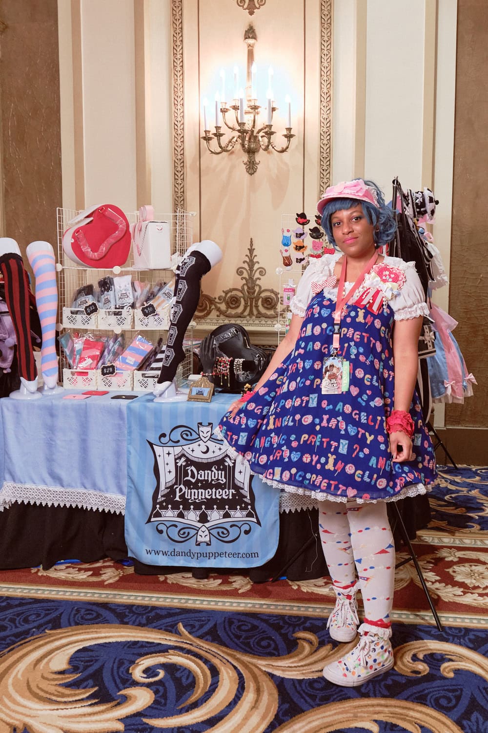 Dandy Puppeteer designer Tiffany wearing sweet lolita, standing in front of her booth.