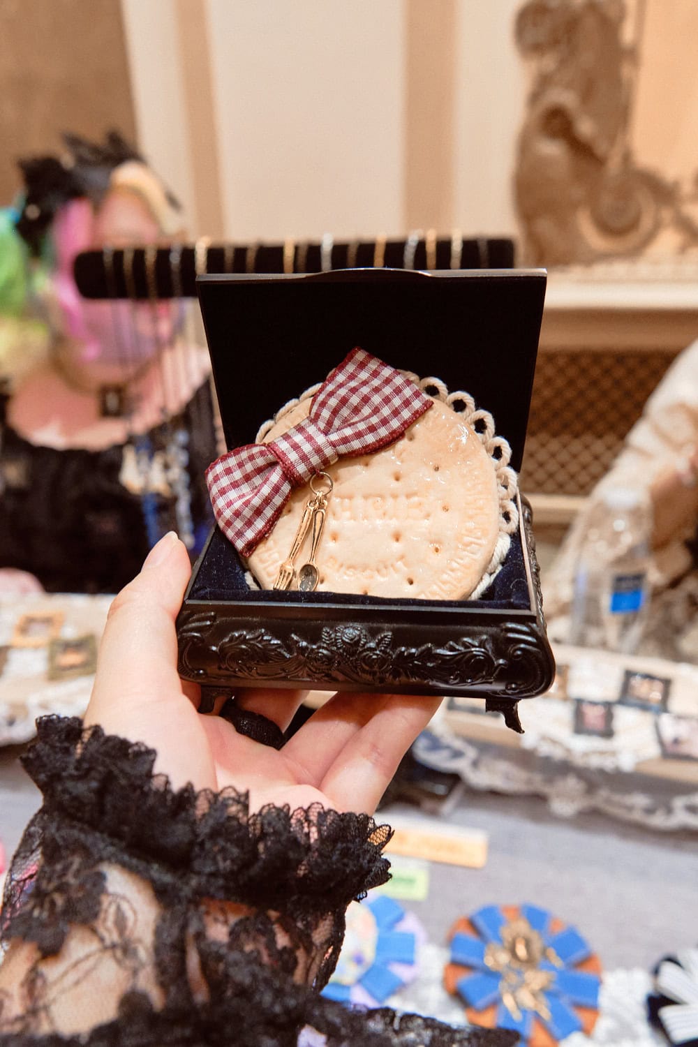 Biscuit shaped brooch with a red gingham bow glued on top. The brooch is in an ornate box.