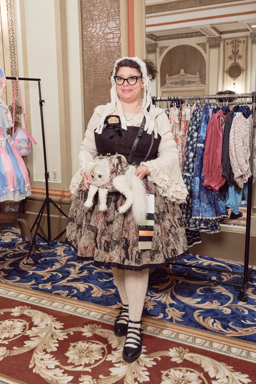 Designer of Mossbadger wearing cream and brown classic lolita outfit featuring a weird cat purse and cat printed gobelin skirt.