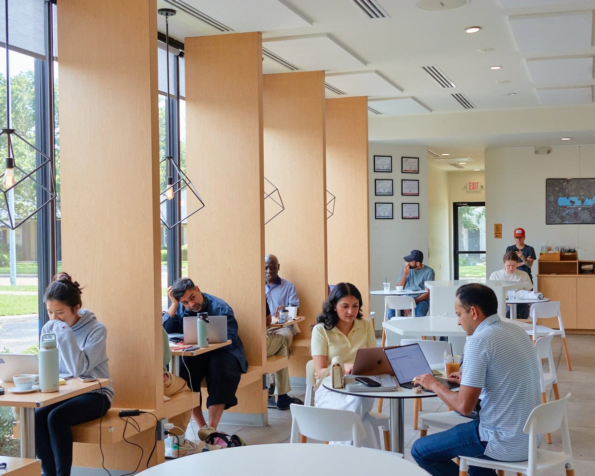 BlendIn Coffee Club interior with booth tables lining the floor to ceiling windows and larger community tables in the center