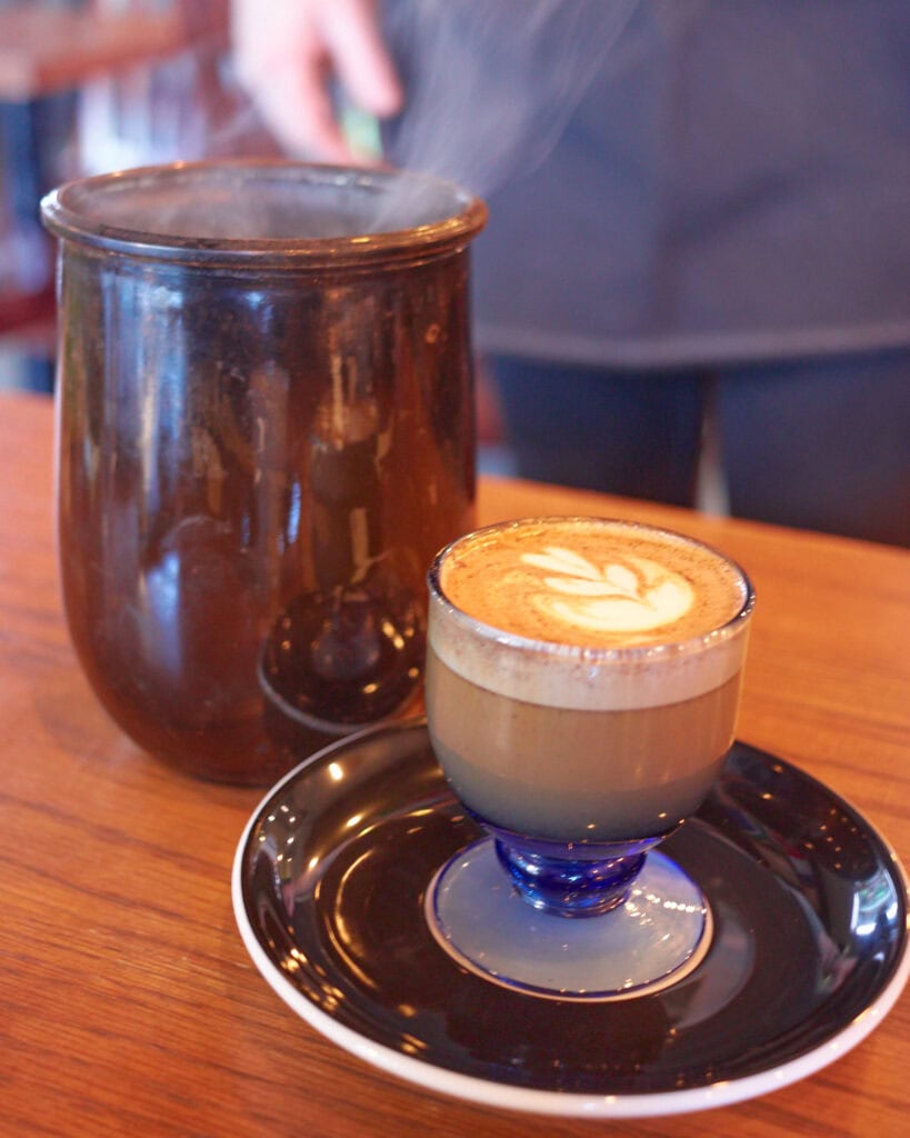 smoked rosemary cortado in a blue glass goblet with smoke coming out of the container